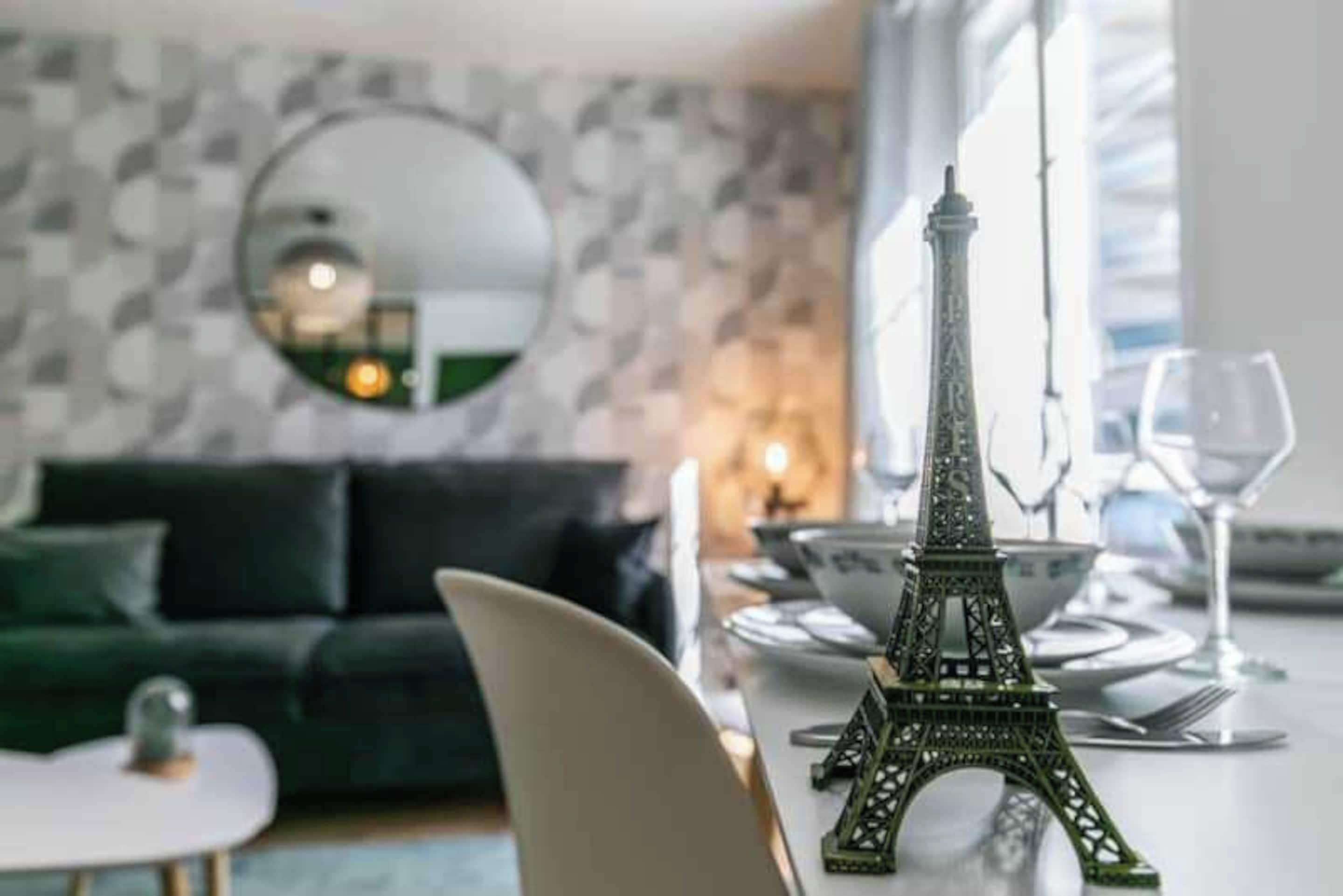A dining area with a table set for two, a decorative Eiffel Tower, a green sofa, and a mirror on the wall.