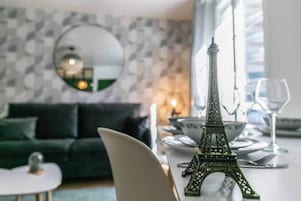 A dining area with a table set for two, a decorative Eiffel Tower, a green sofa, and a mirror on the wall.