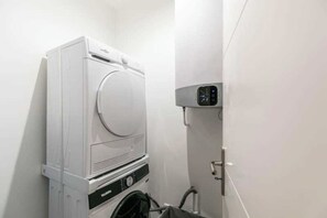 Ein kompakter, moderner Waschraum mit einer übereinander angeordneten Waschmaschine und einem Trockner, einer kleinen Bedienkonsole und einem Schlauch für den Wasseranschluss.