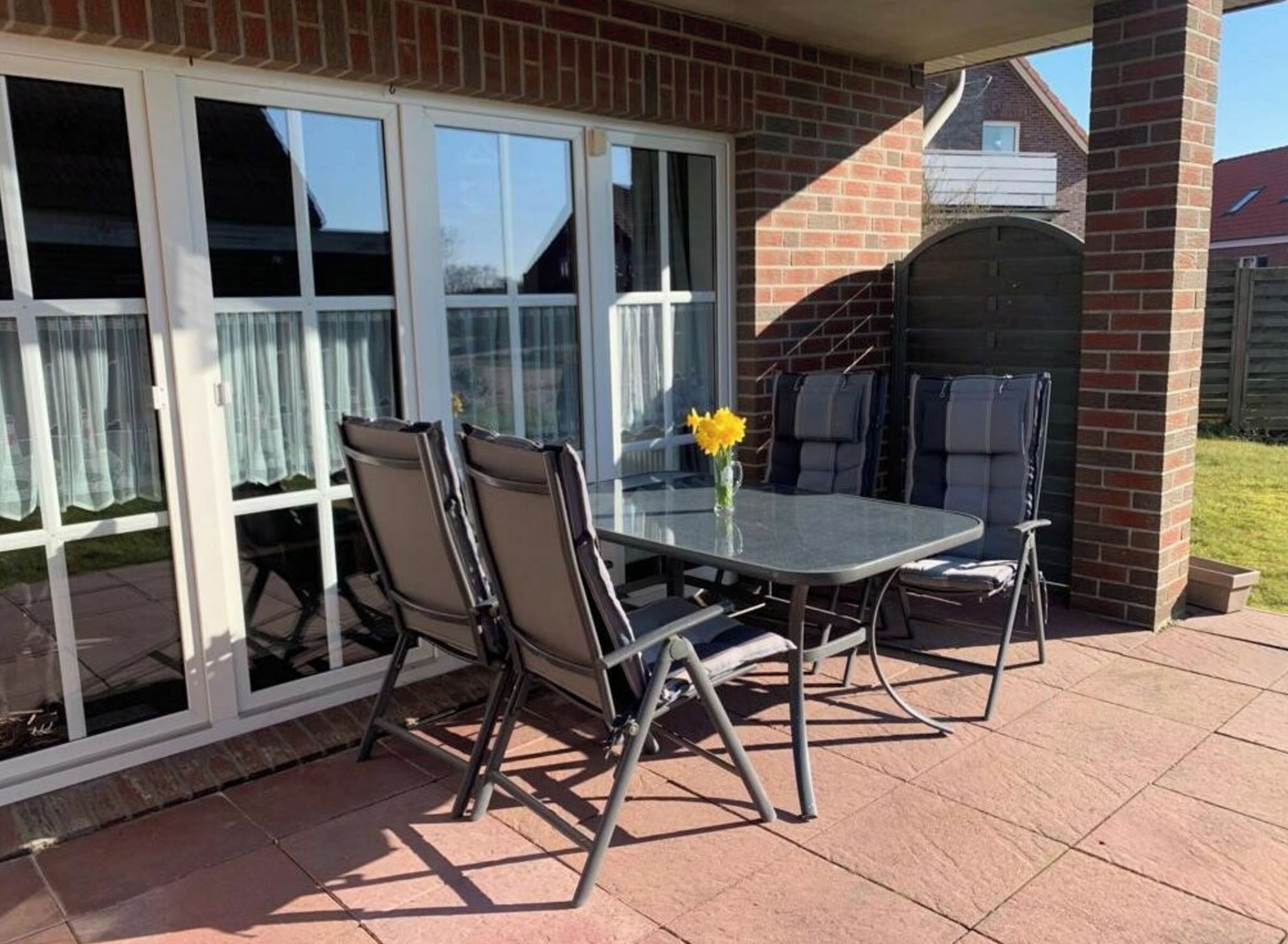 An outdoor patio with a glass table, four chairs, and a barbecue grill.