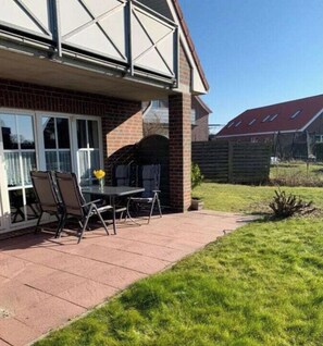 A patio with a table and chairs, a brick wall, and a grassy area. - Holiday Apartment With 2 Bedrooms (Werdum)