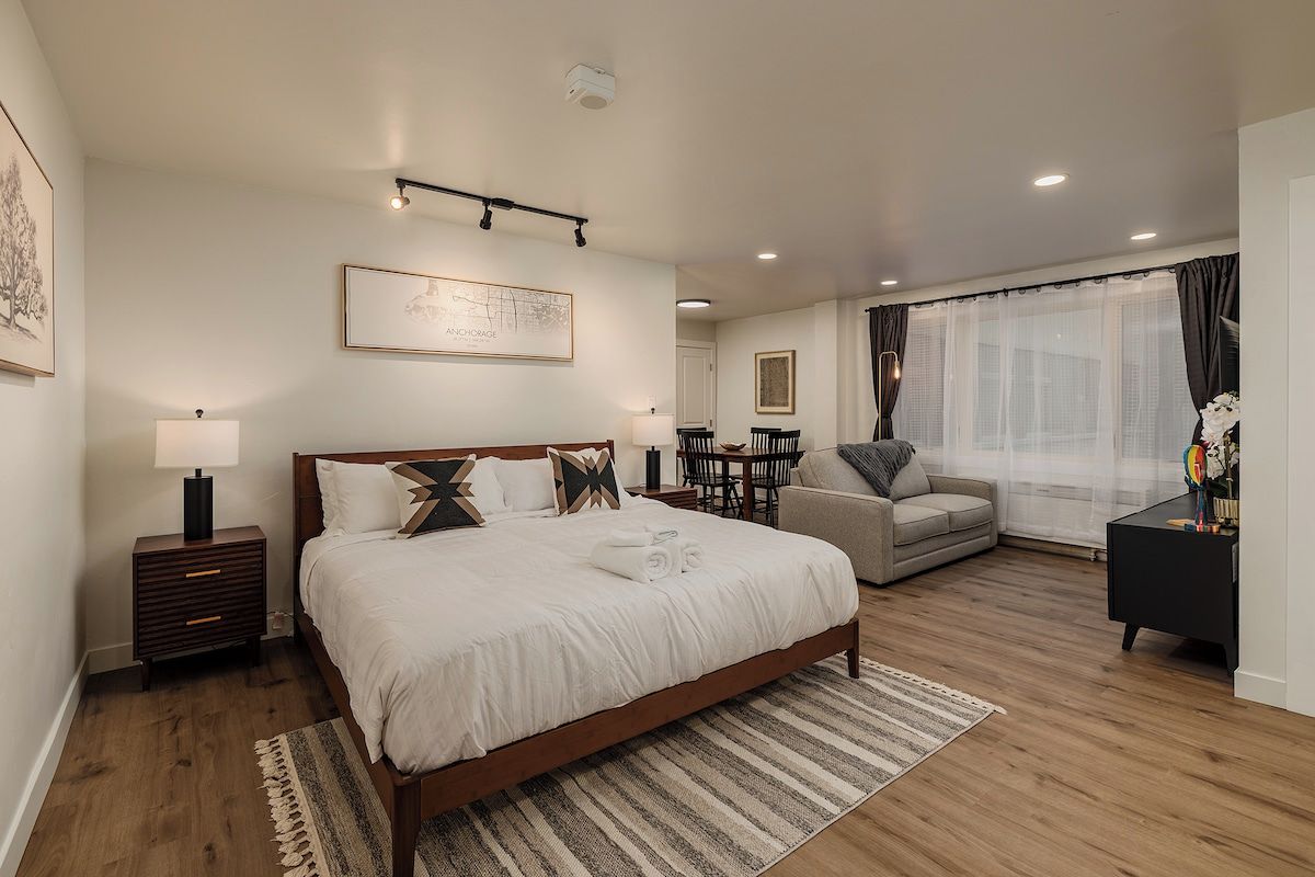 A modern bedroom with a large bed, bedside tables, a sofa, and a dining area.