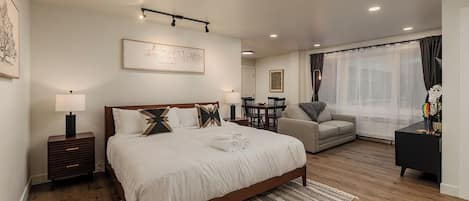 A modern bedroom with a large bed, bedside tables, a sofa, and a dining area.