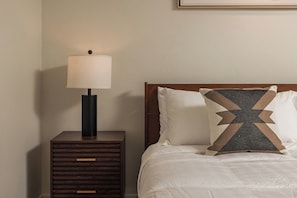 A neatly made bed with a patterned pillow, a bedside lamp, and a wooden nightstand with drawers. - Downtown Anchorage Studio - King Bed -Sleeps 4 (Anchorage)