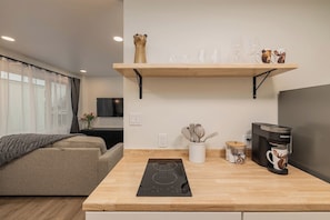 A modern kitchen with a built-in induction cooktop, a coffee maker, and a shelf with decorative items. - Downtown Anchorage Studio - King Bed -Sleeps 4 (Anchorage)