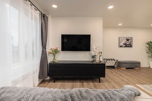 A modern living room with a flat-screen TV mounted on the wall, a black entertainment unit, a grey ottoman, and a potted plant. - Downtown Anchorage Studio - King Bed -Sleeps 4 (Anchorage)