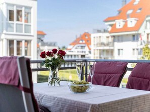 A table set for dining with a vase of flowers and a bowl of grapes, overlooking a residential area with houses. - Holiday Apartment With 2 Bedrooms (Grossenbrode)