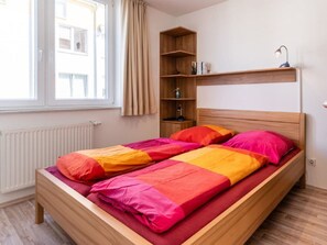 A bed with a wooden headboard, a bedside shelf with books, and a window with curtains. - Holiday Apartment With 2 Bedrooms (Grossenbrode)