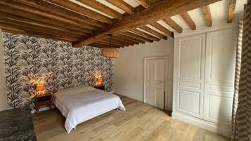 Un dormitorio con cama, techo de madera, papel tapiz estampado, puerta blanca y cortina a rayas.