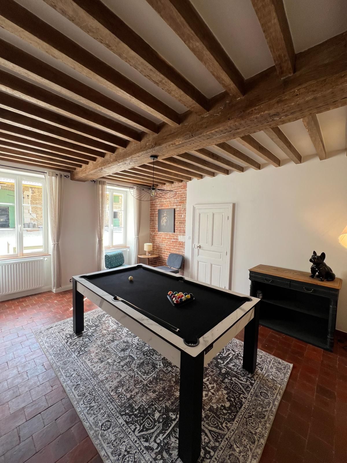 A room with a pool table, a brick wall, and a wooden ceiling.