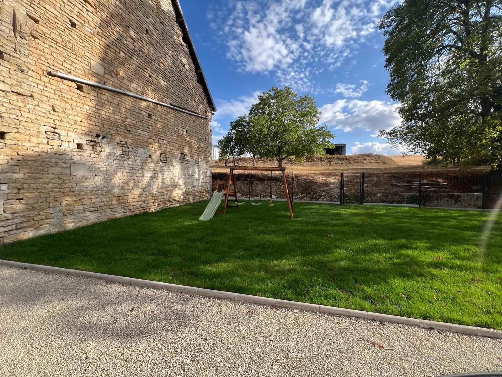 Un espacio al aire libre con césped, una pared de ladrillo, un columpio y un tobogán.