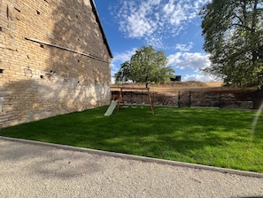 A grassy outdoor area with a brick wall, a swing set, and a slide.