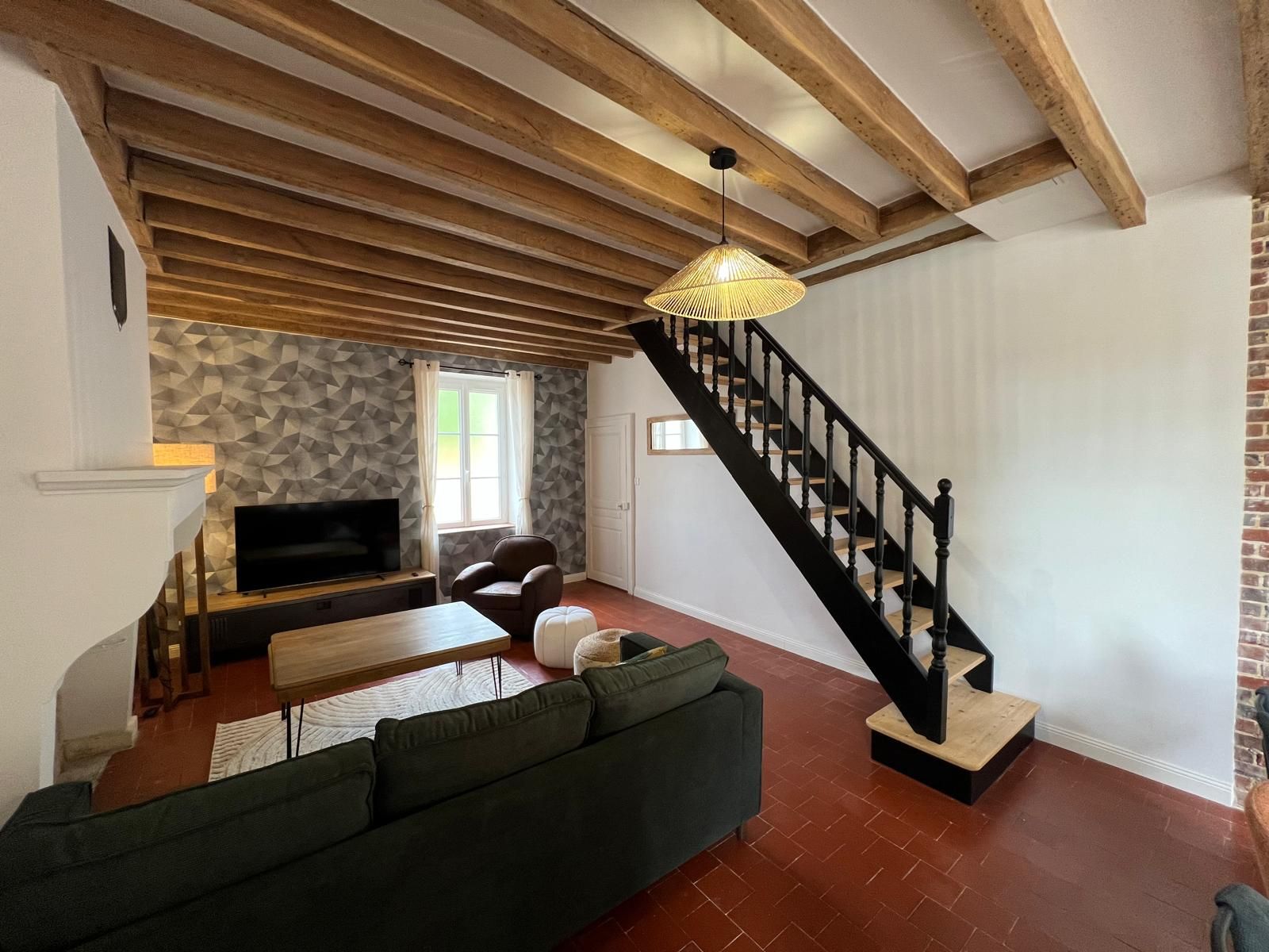 A living room with a sofa, a TV, a staircase, and a patterned wall.