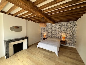 A bedroom with a wooden ceiling, a fireplace, a bed, and patterned wallpaper.