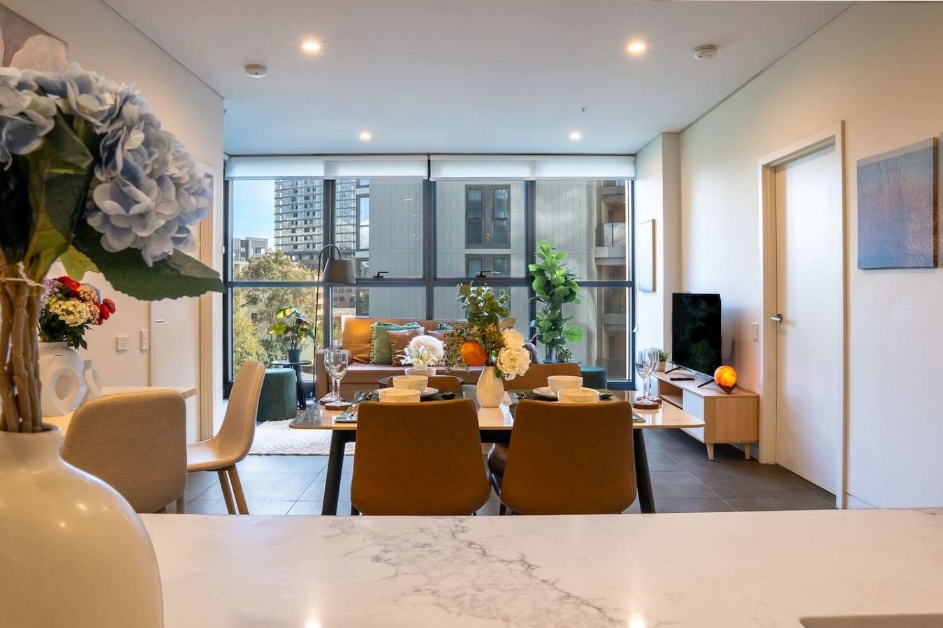 A modern dining area with a marble table, chairs, and a city view through large windows.