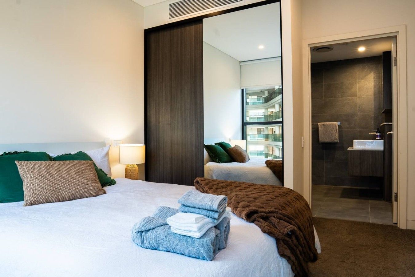 A hotel room with a bed, a mirror, a bathroom, and a view of the building's interior.
