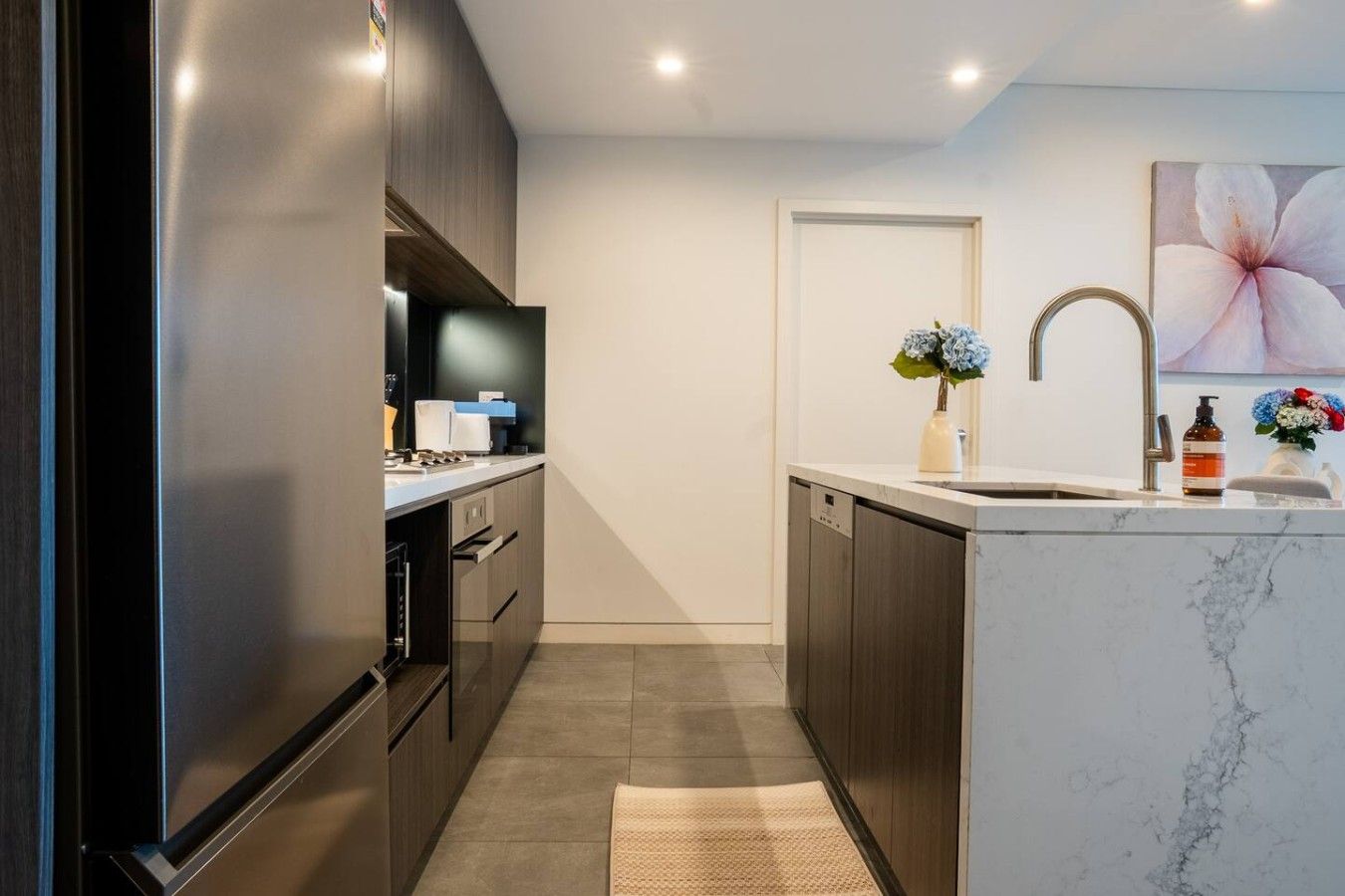 A modern kitchen with dark cabinetry, a marble countertop, and a built-in dishwasher.