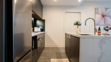 A modern kitchen with dark cabinetry, a marble countertop, and a built-in dishwasher.