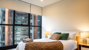 Een moderne hotelkamer met een groot raam, een bed met een bruine deken, twee kussens en twee bedlampen.