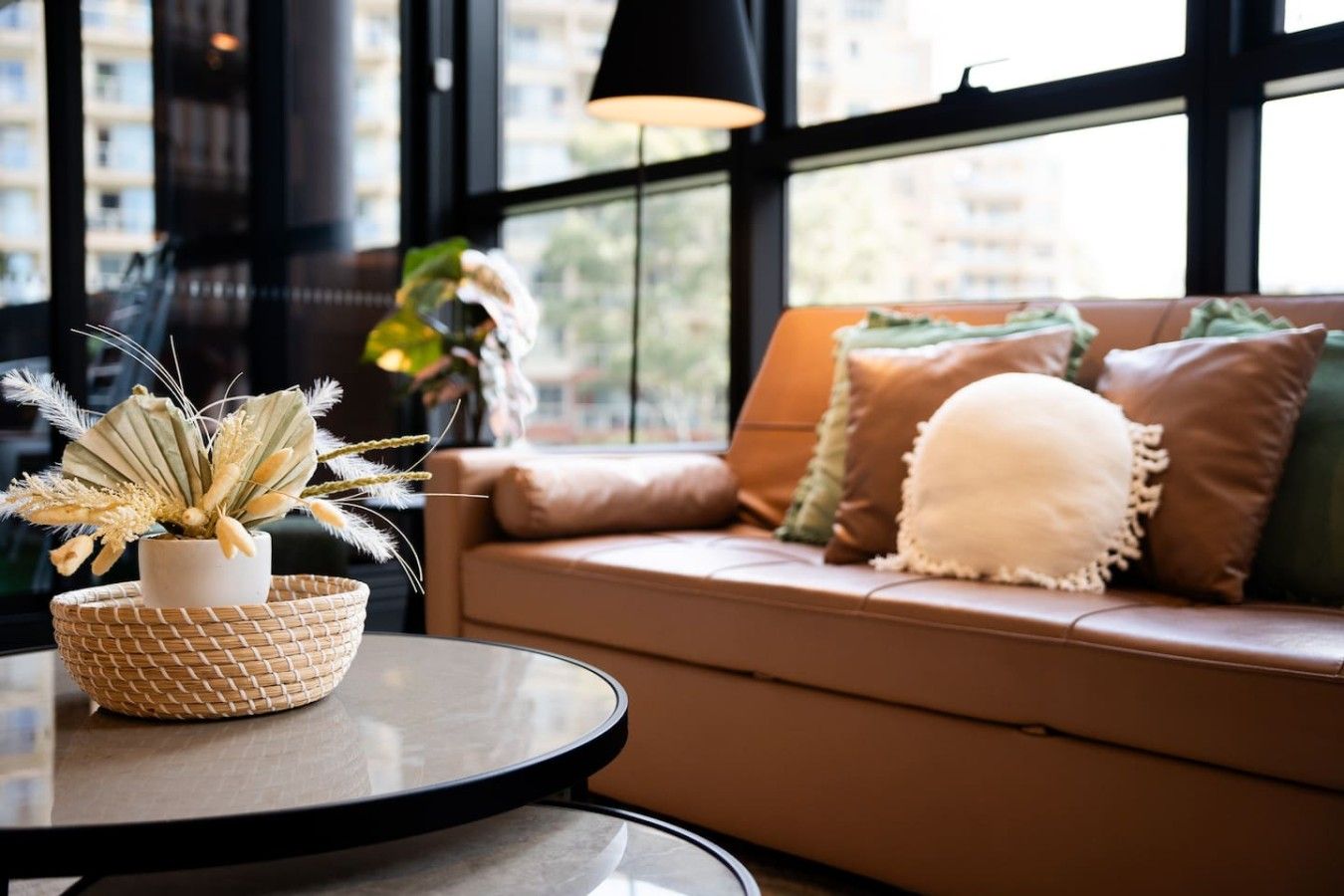 A modern living room with a round glass table, a potted plant, and a sofa with multiple cushions.