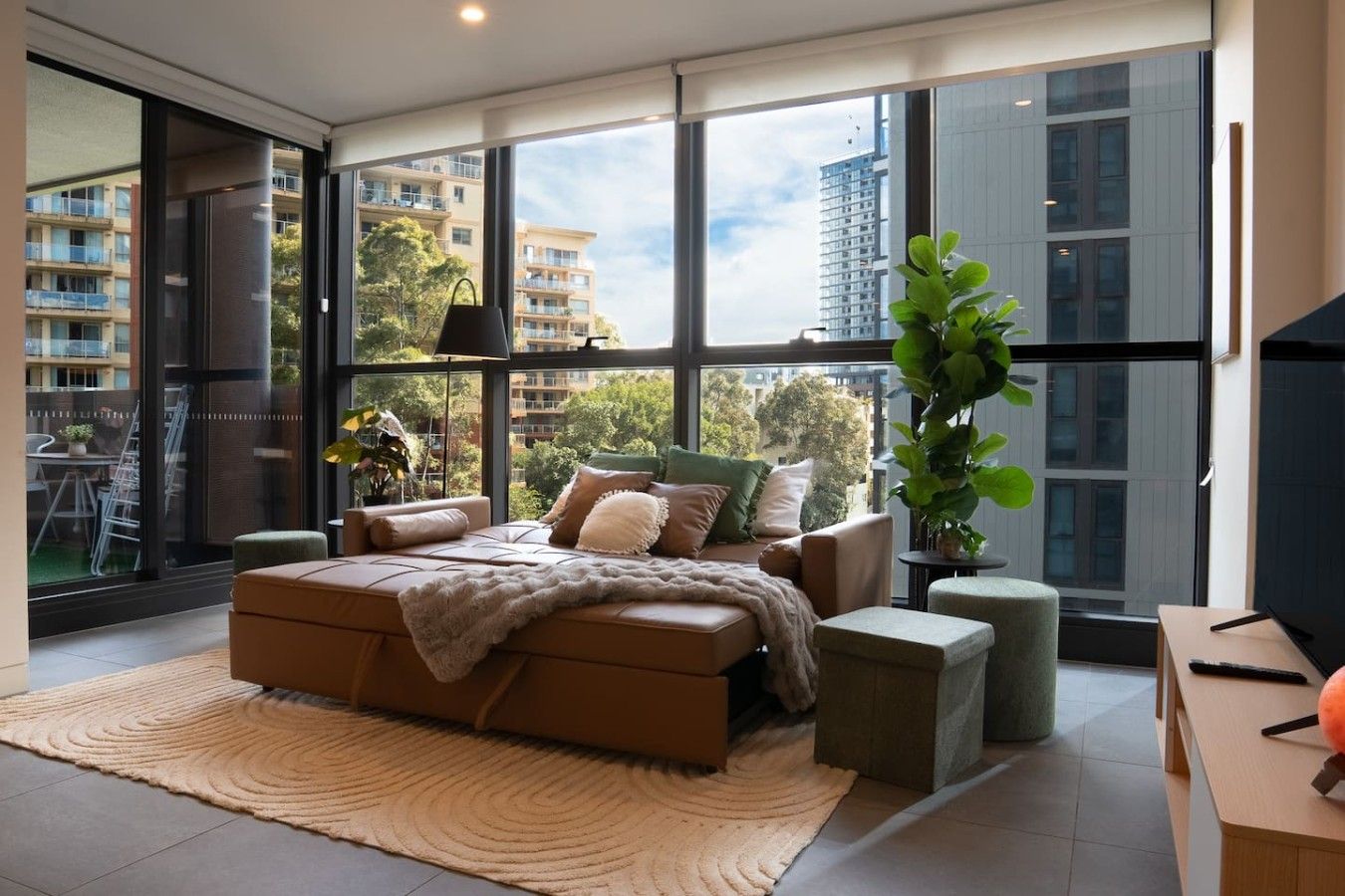 A modern bedroom with a large bed, a view of the city, and a potted plant.