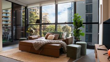 A modern bedroom with a large bed, a view of the city, and a potted plant.