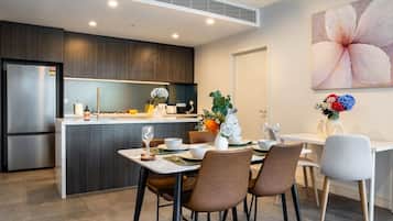 A modern kitchen with a built-in refrigerator, a dining area with a table set for two, and a large flower painting on the wall.