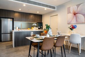 A modern kitchen with a built-in refrigerator, a dining area with a table set for two, and a large flower painting on the wall. - Stylish Homebush Retreat | BBQ, Gym & Parking (Homebush)