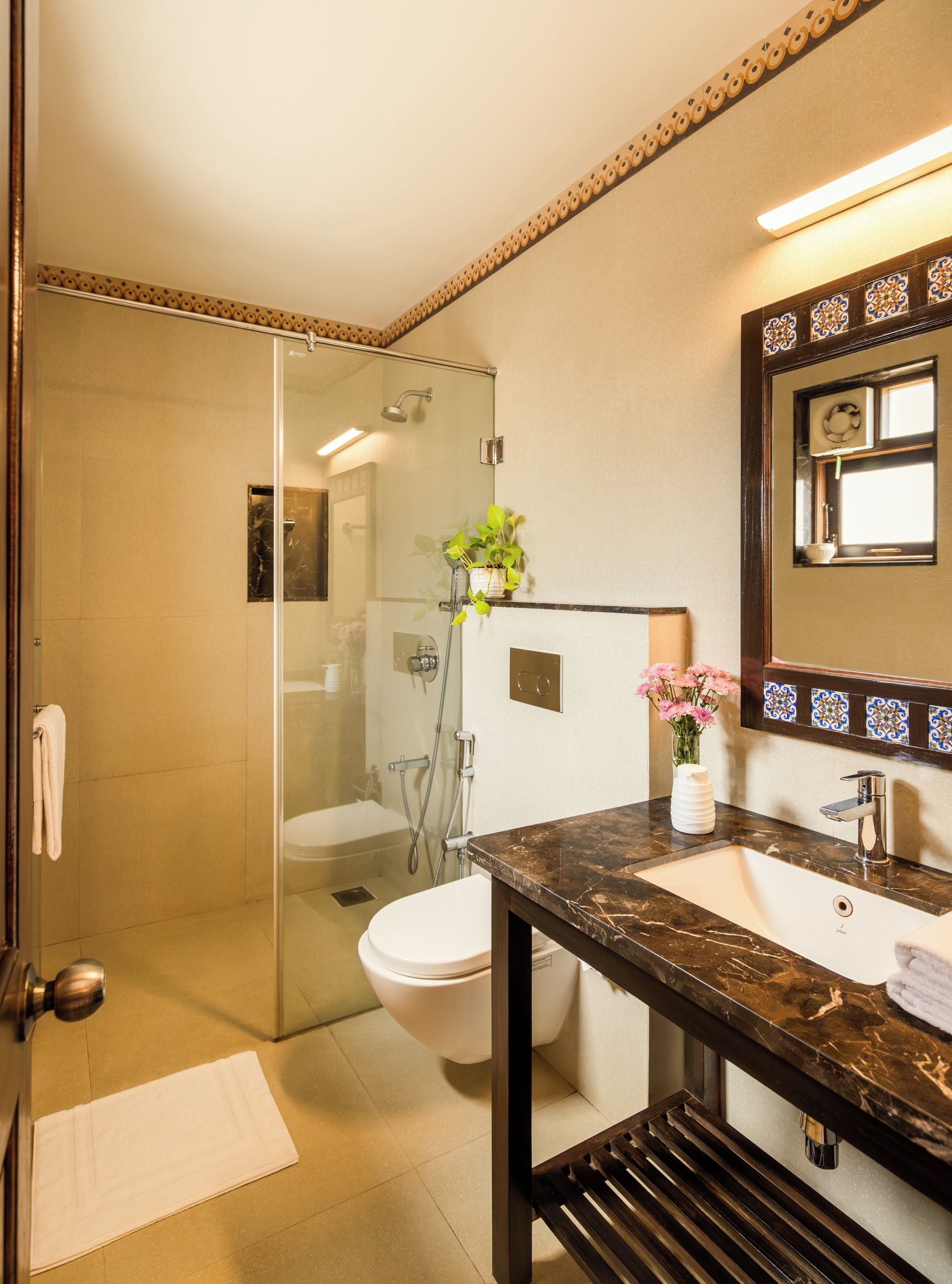 A modern bathroom with a glass-enclosed shower, a white toilet, a marble sink, and a mirror with decorative tiles.