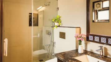 A modern bathroom with a glass-enclosed shower, a white toilet, a marble sink, and a mirror with decorative tiles.
