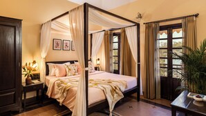 Ein Bett mit Baldachin, Nachttische, ein Beistelltisch, ein Fenster mit Vorhängen und ein Deckenventilator.