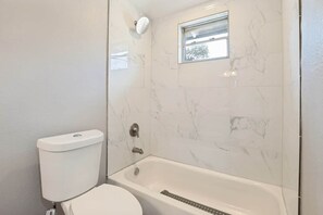 A bathroom with a toilet, a bathtub, and a showerhead. - Lancaster Town Square House Near Downtown Dallas (Lancaster)