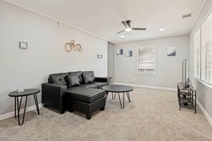 A room with a sectional sofa, two side tables, a ceiling fan, and a window with blinds. - Lancaster Town Square House Near Downtown Dallas (Lancaster)