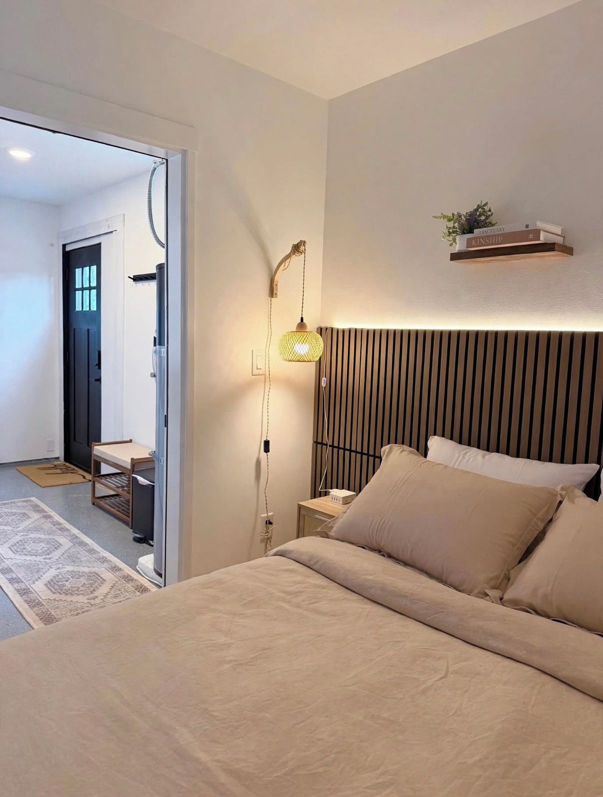 A bedroom with a bed, bedside table, lamp, and a shelf with a plant.