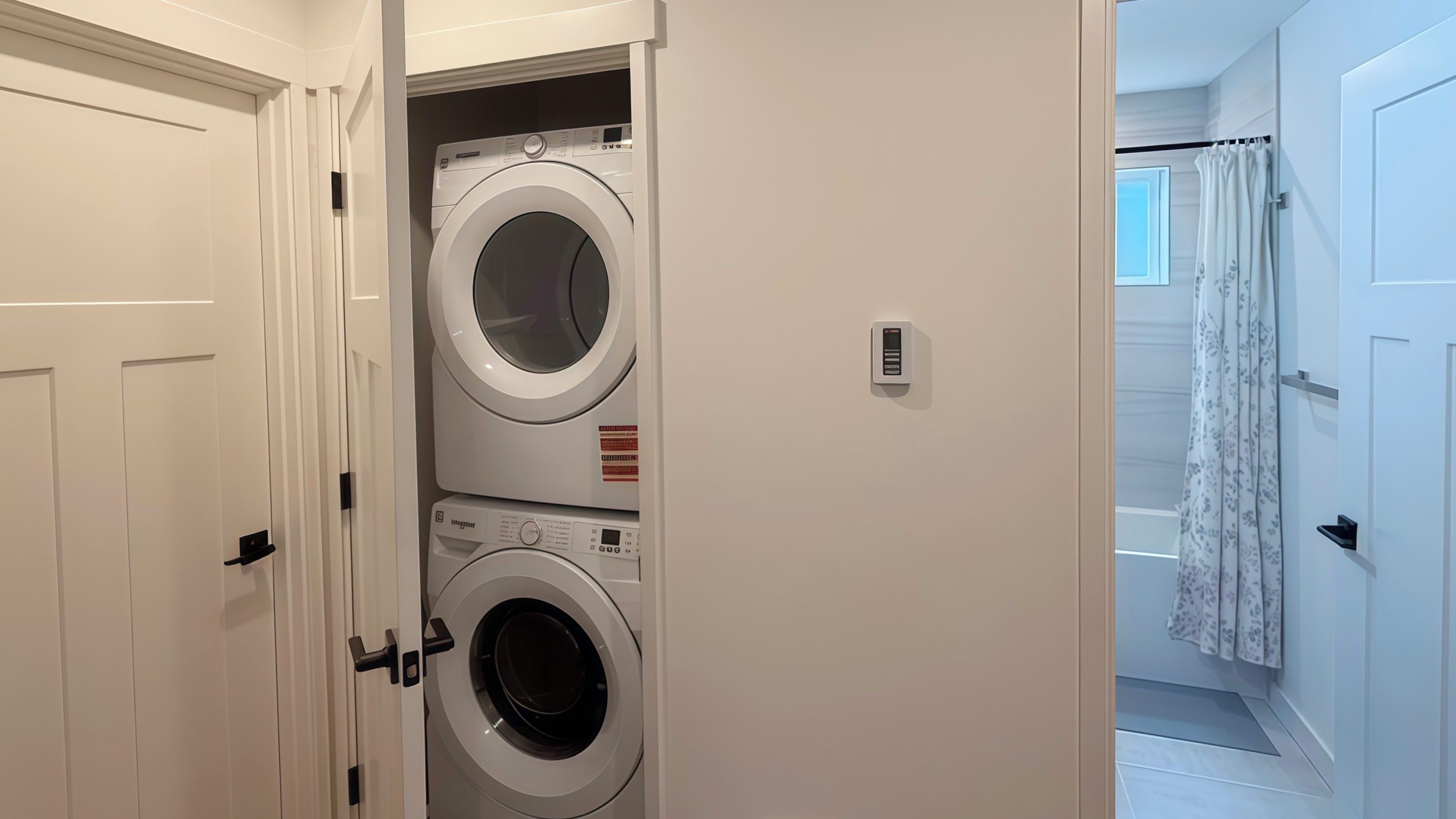 A laundry room with two stacked washing machines and a control panel.