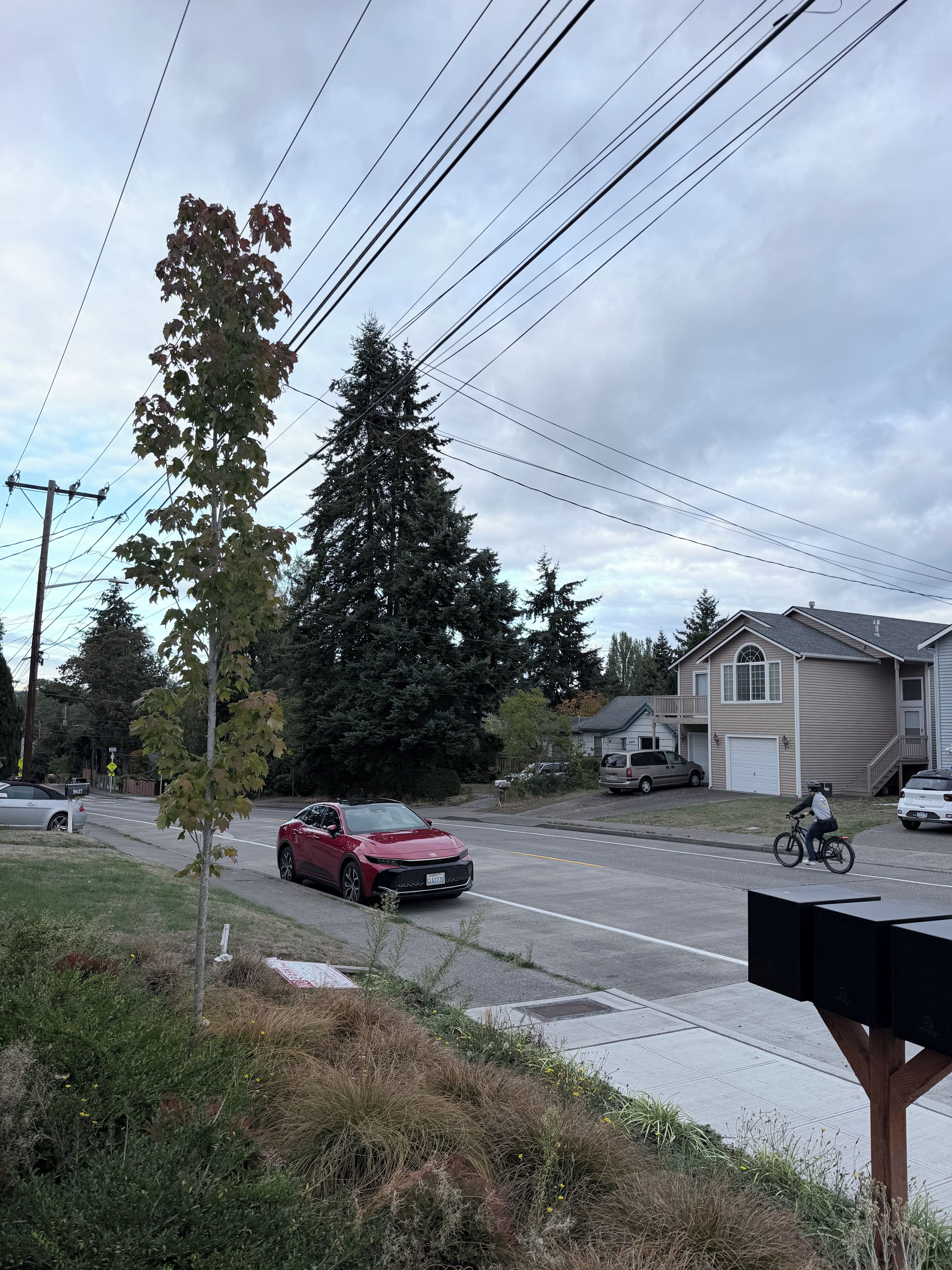 A residential street with houses, a parked car, and a cyclist.