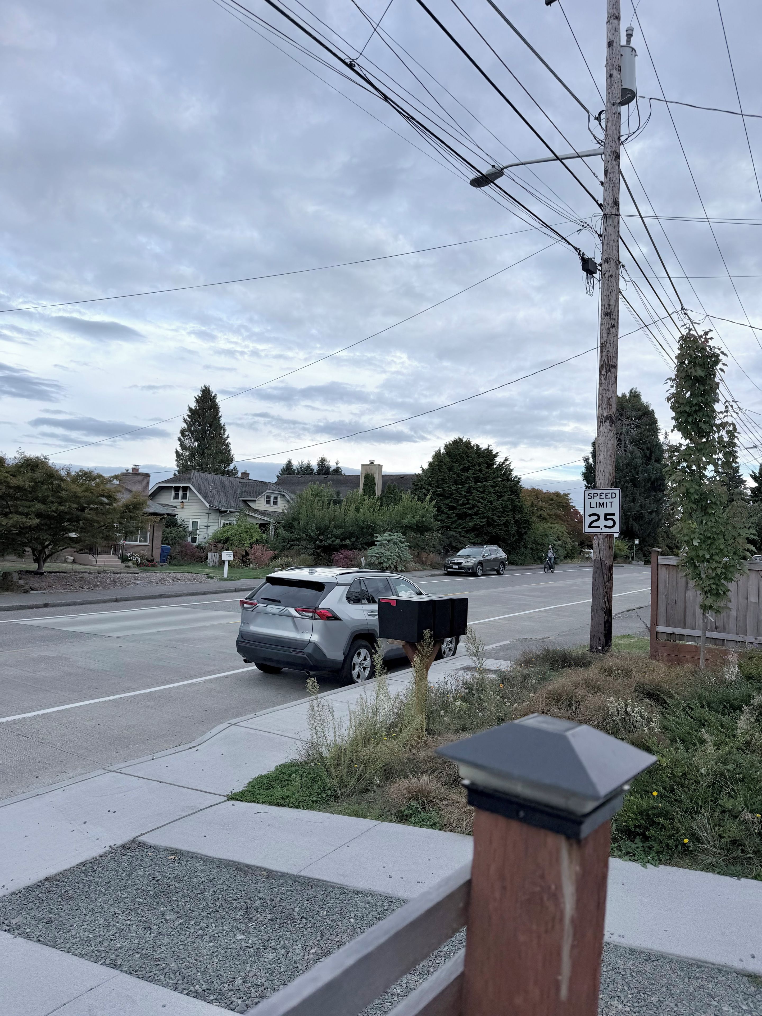 A residential street with houses, a speed limit sign, and a parked SUV.