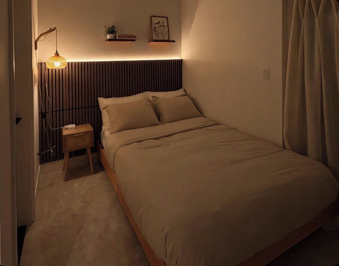 Et soveværelse med seng, sengebord, lampe og vægmonteret hylde med en plante.