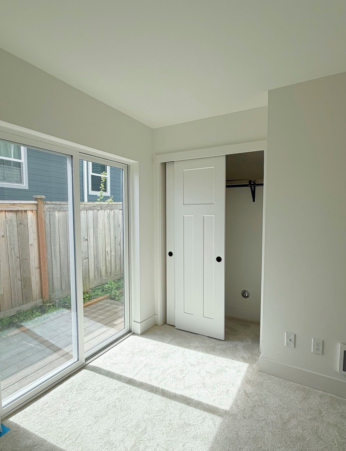 Quarto com porta de vidro deslizante para um pátio, armário branco com porta e piso coberto de carpete.
