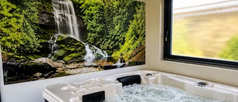 Un jacuzzi con un mural de cascada, una ventana con vistas y una bañera con panel de control.