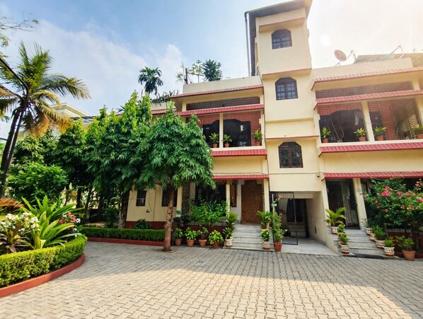 A multi-story building with a paved courtyard, surrounded by lush greenery and potted plants.