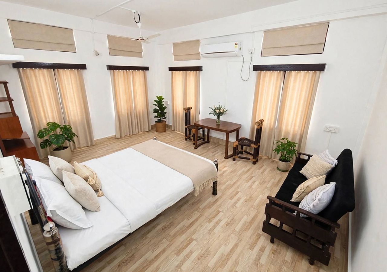 A hotel room with a bed, a sofa, a dining table, and potted plants.