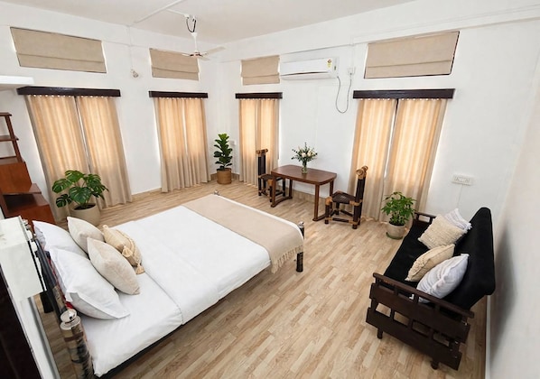 A hotel room with a bed, a sofa, a dining table, and potted plants. - Vandara Oasis | King Size Bed AC Room (Guwahati)