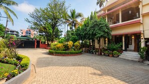 Une cour avec un chemin pavé, entourée de verdure et de palmiers, qui mène à un bâtiment doté d’un toit rouge et de plusieurs balcons.