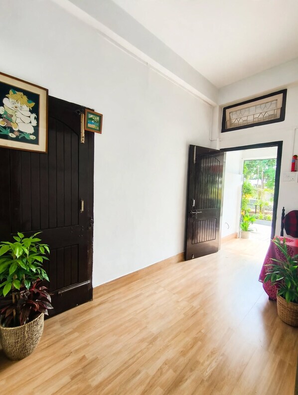 A hallway with a wooden floor, a black door, and a view of greenery outside.