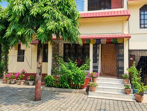 A building with a covered entrance, potted plants, and a tiled pavement.