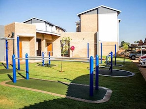 A playground with blue exercise equipment, a building with a flat roof, and a clear sky.