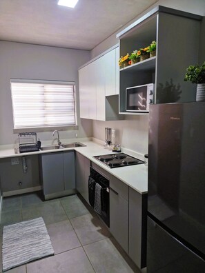 A compact kitchen with a built-in microwave, a stainless steel refrigerator, and a window with blinds. - Modern 2 Bedroom Apartment (Pretoria)