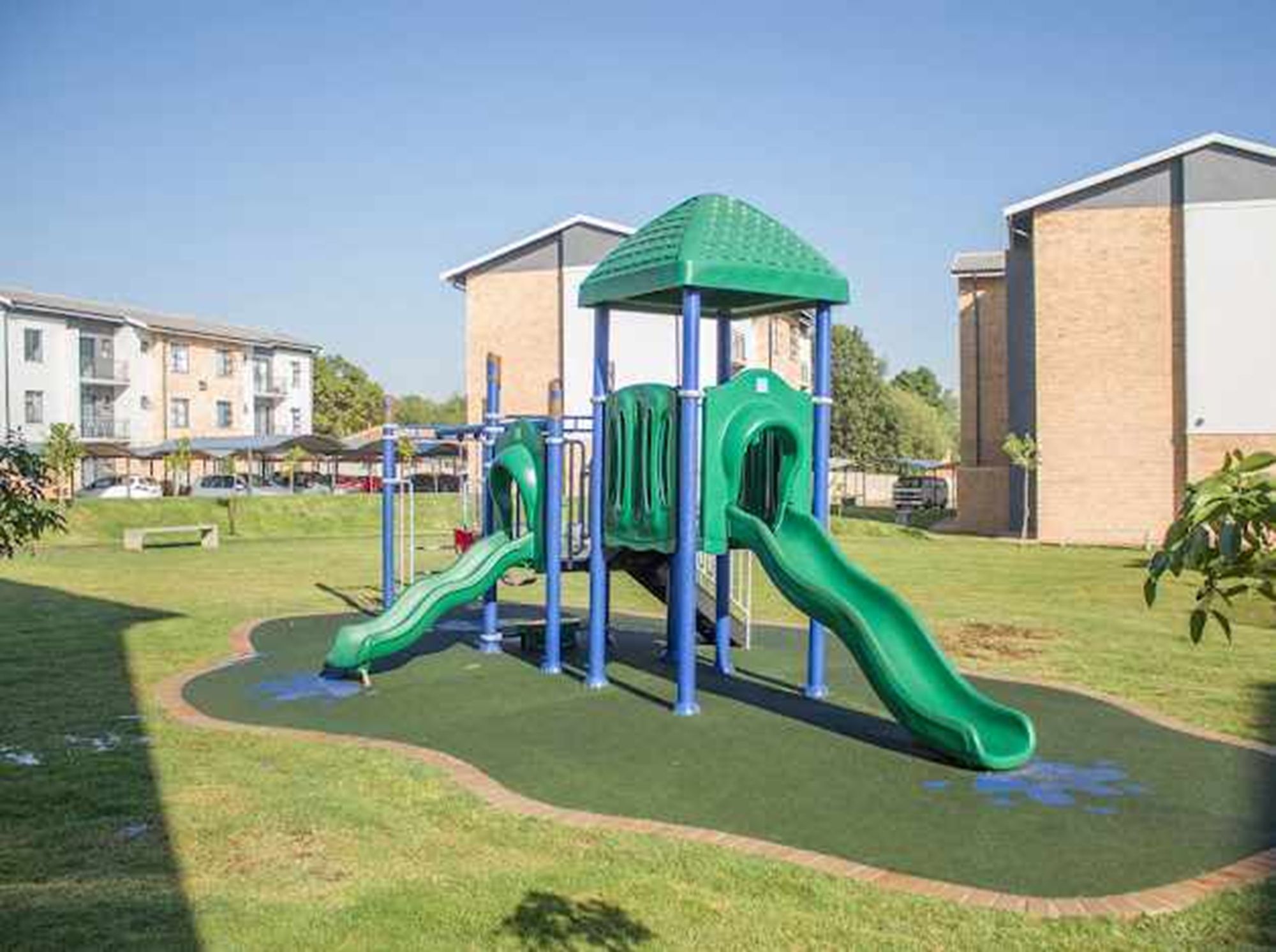Un’area giochi con scivoli e strutture per arrampicata, circondata da un prato e palazzi residenziali.
