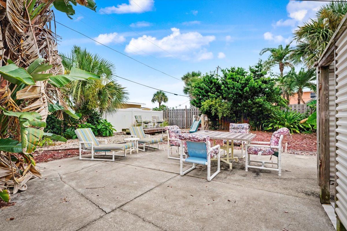 Eine Terrasse mit Gartenmöbeln, darunter ein Tisch und Stühle, umgeben von Pflanzen und einem Holzzaun.